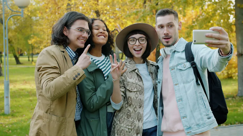 Four friends capturing a happy moment with a selfie in a vibrant autumn park.